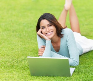 Smiling hispanic girl with laptop lying on grass